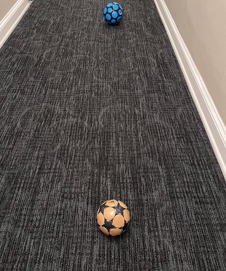 Two soccer balls sit in  vertical line in a hallway.