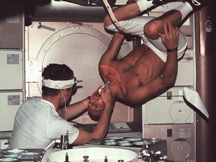 Two people are inside the Skylab space station. One is shirtless and floating upside down. 