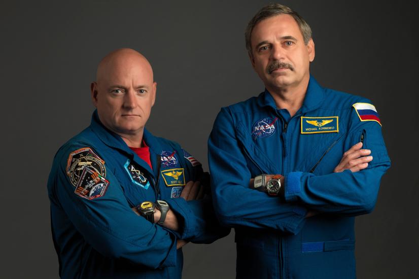 Two astronauts in blue jump suits with their arms crossed stare into camera. 