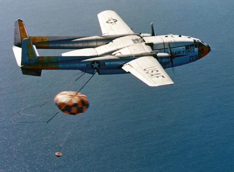 An Air Force plane with a parachute of a satellite recovery vehicle flying over the ocean.