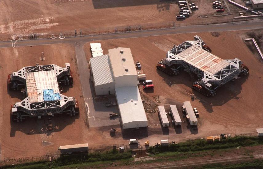 Two giant mobile launch crawlers seen from above next to a building.