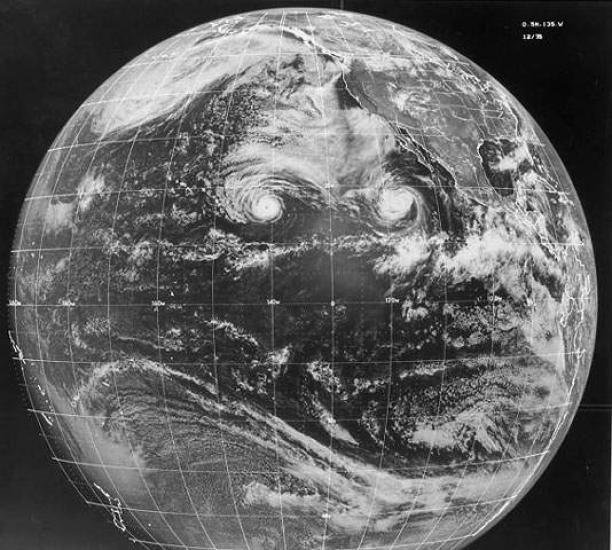 A black and white image of the earth with two swirling storms seen on its surface.