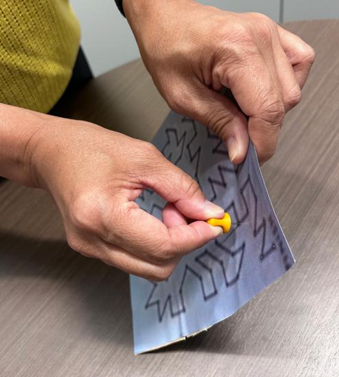 A photograph of a hand pushing a push pin through a maze print out. 