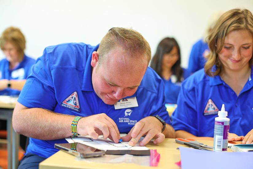 An educator in a blue polo shirt leans close to the table focusing on a task. 