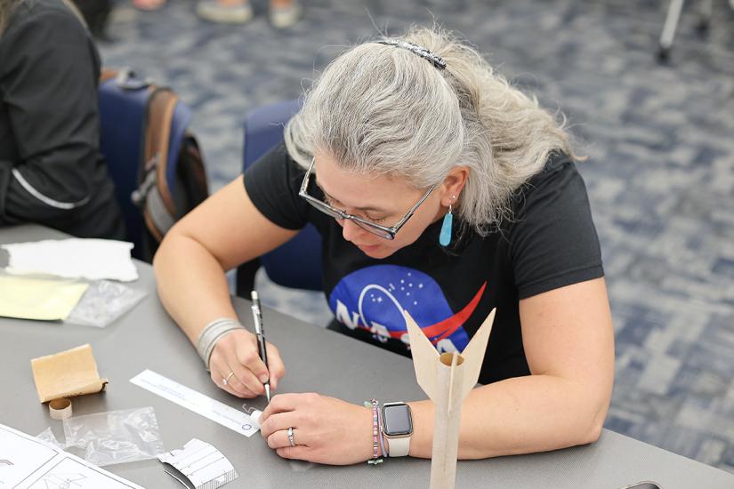 A person in a NASA tee shirt leans closer to the table focusing on a task. 