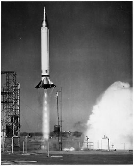 A rocket taking off from its launch pad. The rocket is a light color and looks to have just left the ground. Smoke bellows up from below the rocket.