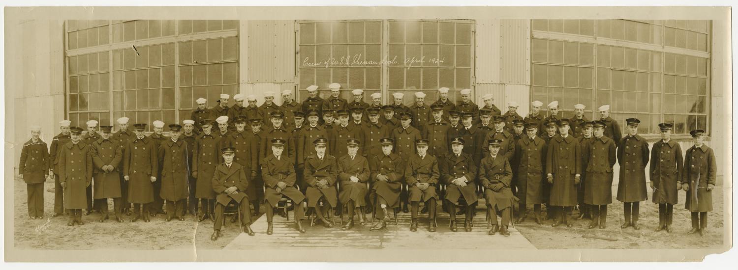  A partial view of a photograph of the entire crew of the USS Shenandoah in April 1924. A row of men sit posed in front of the camera with two rows of men standing behind them.