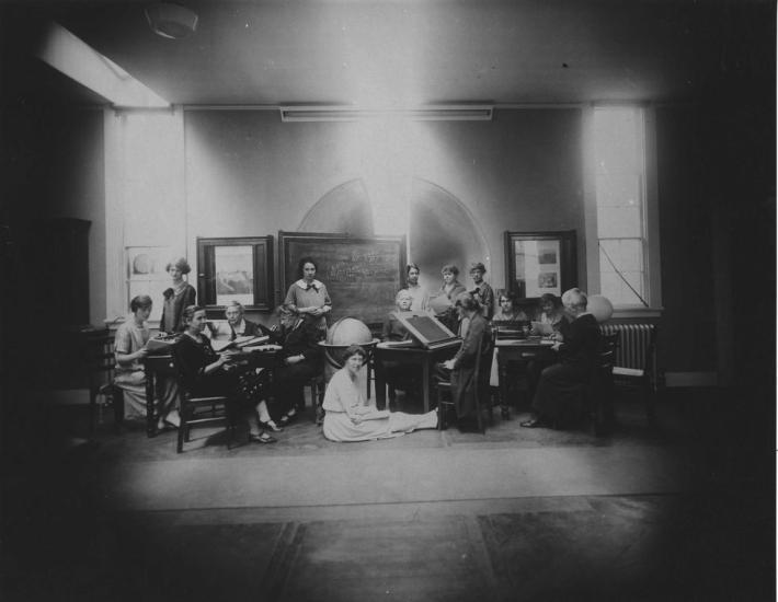 An old photograph of women in a classroom with a chalkboard and globes. 