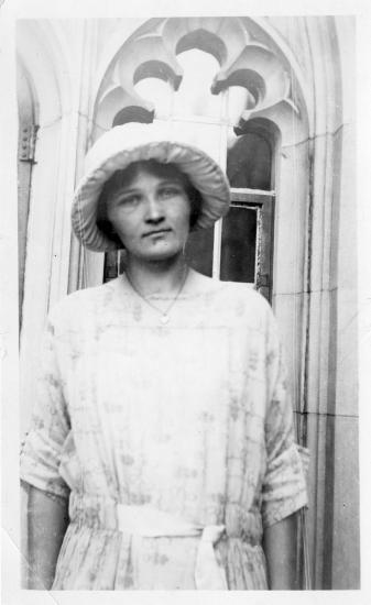 A woman with a hat stands in front of an architectural exterior. 