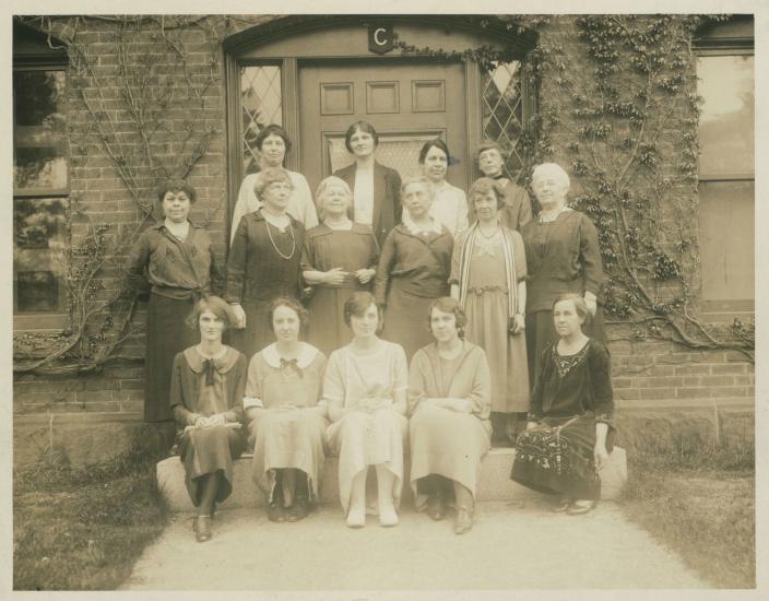 Several older women stand in front of a door in a sepia tone photograph.