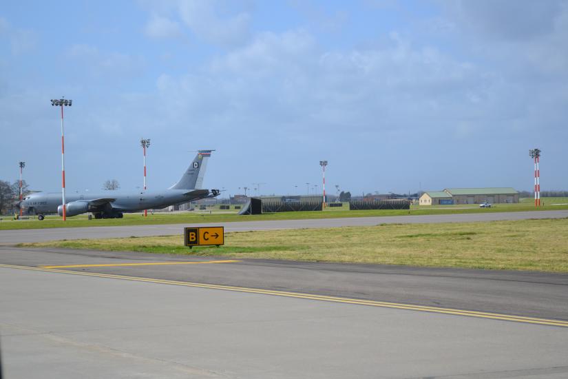 A large aircraft on a runway where a taxiway sign is visible.