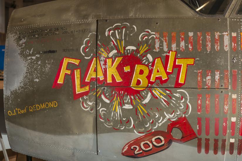 On the side of a bomber, the name "Flak-Bait" is painted, as well as an icon of a bomb with the number 200 on it and the name "O.J. Red Redmond."