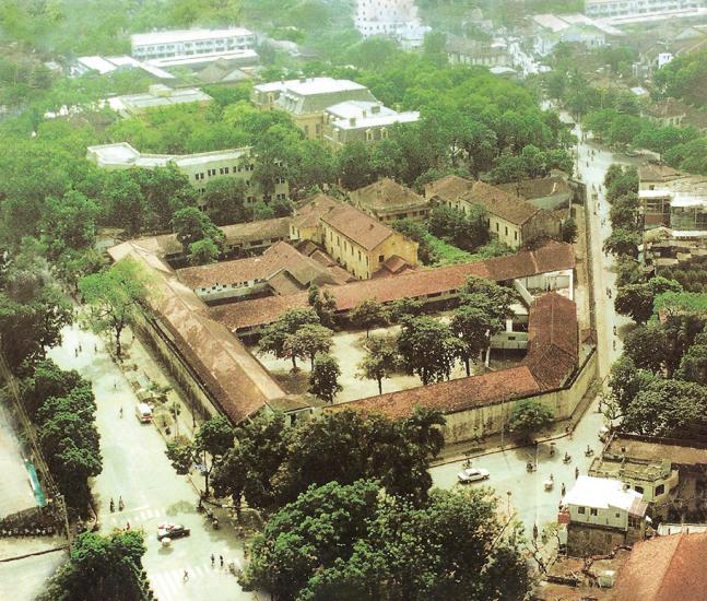 Aerial view of a buiding with red-tiled roofs in an urban setting. City streets and green trees surround the building.