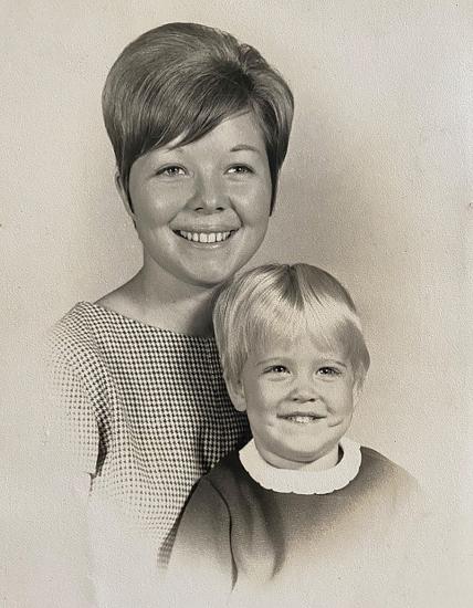 A black-and-white photograph of a young woman with short dark hair styled in a 1960s fashion and a four-year-old girl with short blond hair. Both the woman and child are smiling.