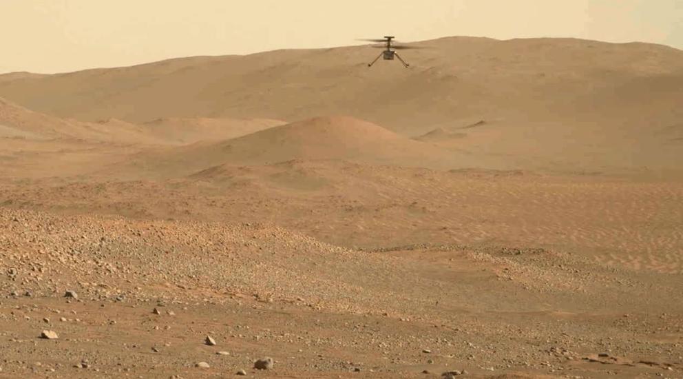 A small helicopter seen in the distance flying above the surface of Mars.