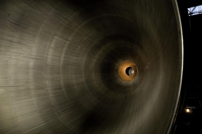 A photo looking into the base of a large metal, hollow, cone, which takes up the majority of the frame. At the point of the cone the metal changes to a rust and orange type color. 