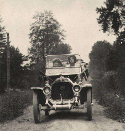 A grainy black and white photograph of two women in a car in 1910. 