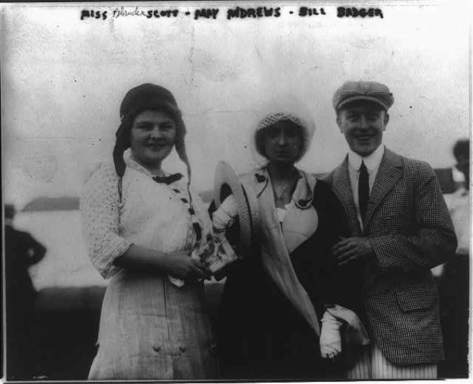 A woman on the left wears an an aviator's hat, she stands next two a woman and a man. 