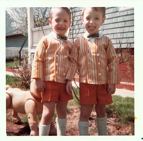 Two three year old boys in the 1960s. They wear matching orange short and striped orange blazers. 