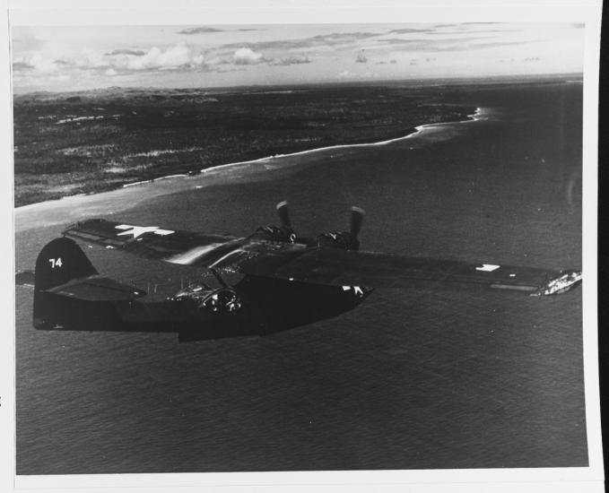 Small dark-colored plane flying over water.