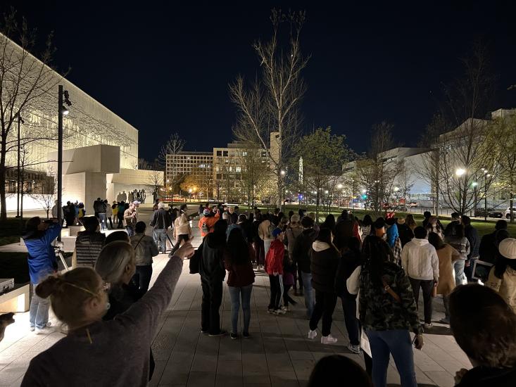 A group outside at night looking at the sky surrounded by faintly lit trees and buildings