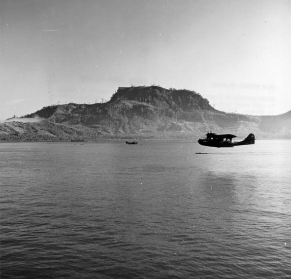 Wide view of an aircraft flying over water in the distance.