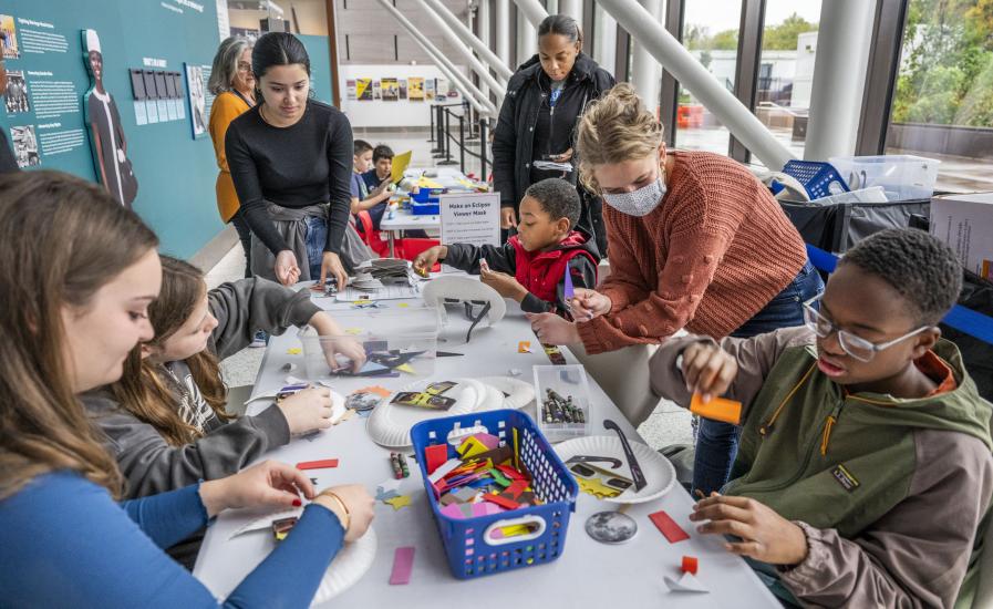 Young visitors sit at a table, decoration eclipse viewers, while assisted by adults. 