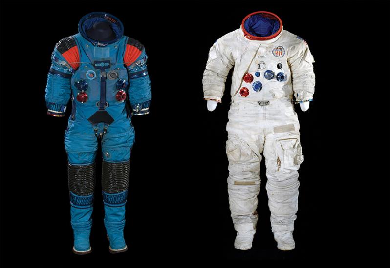 Left: An empty blue spacesuit with black rubber material surrounding the knees and black and bright red material at the shoulders. Right: An white empty Apollo moonsuit is slightly smudged with dust.