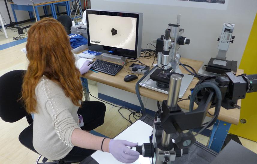 A woman sitting at a computer desk with a microscope device attached to it.