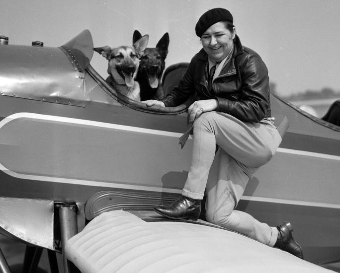 Woman poses on one knee on the wing of an aircraft.