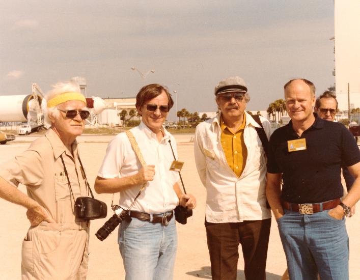 Four men pose for a picture outdoors.