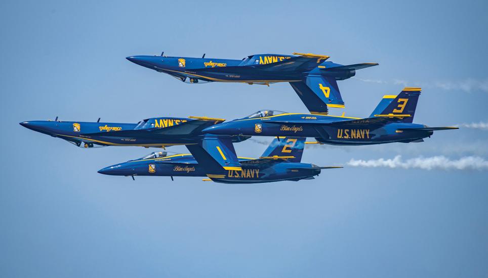 Four military jets fly in a tight formation. Two of the jet aircraft are flying inverted. The jets are painted blue--with yellow letters saying: U.S. Navy.