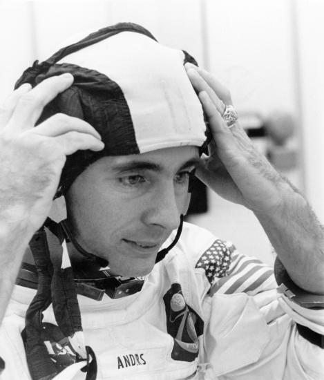 Astronaut William Anders, wearing a white Apollo spacesuit,  adjusts his snoopy cap during preparations for the Apollo 8 mission.