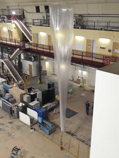 A large hot air balloon attached to a small rocket inside of a facility.