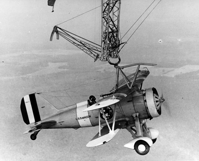 A small monoplane hangs from a hook high in the sky.