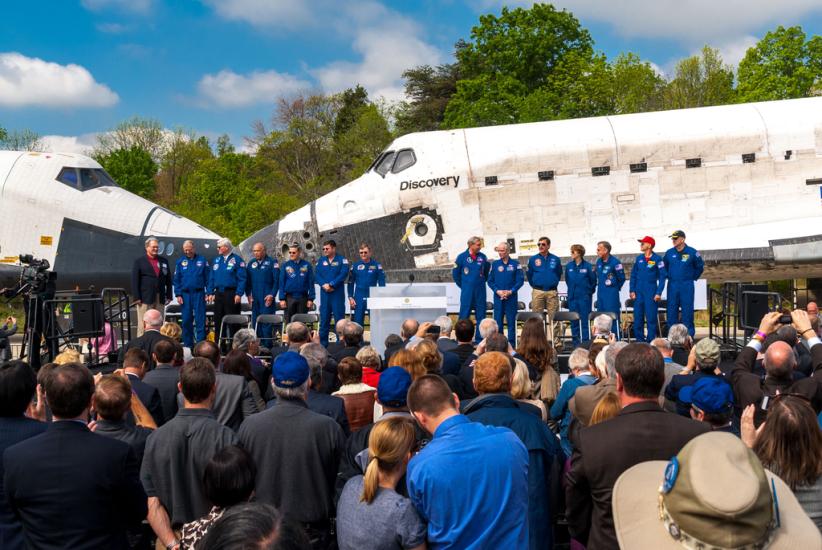 A group of astronauts stand next to two space shuttles that are nose to nose.