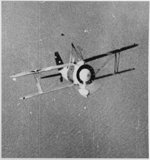 Biplane flies over water. The photo is taken from right in from of it while it is banked upwards. 