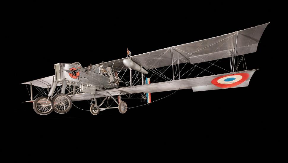 An enormous silver biplane with a large forward cockpit compartment. On the underside of the lower wing is a red, white, and blue roundel marking.