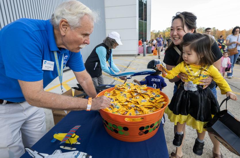 A woman lifts a small child dressed like the Wiggles to grab candy from a bucket