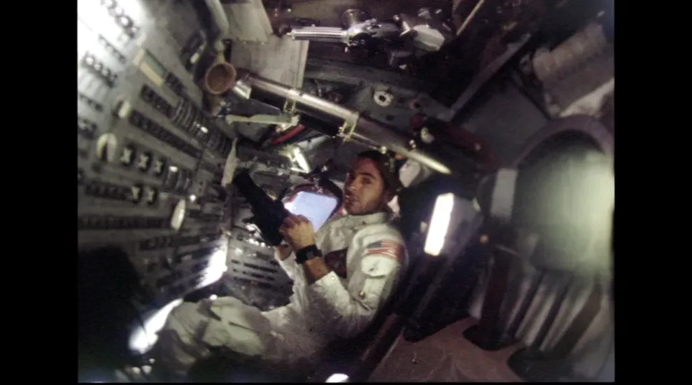 An astronaut holding a camera whiling inside of a command module.