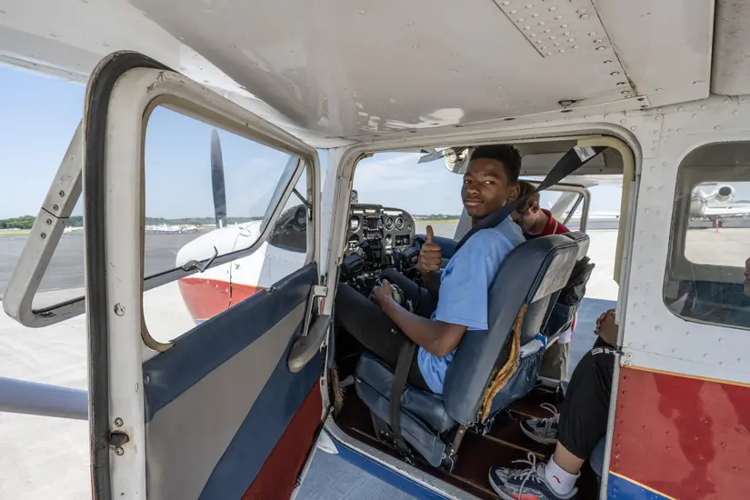 A young man sits in the cockpit of a small aircraft. He gives the photograph a thumbs up.
