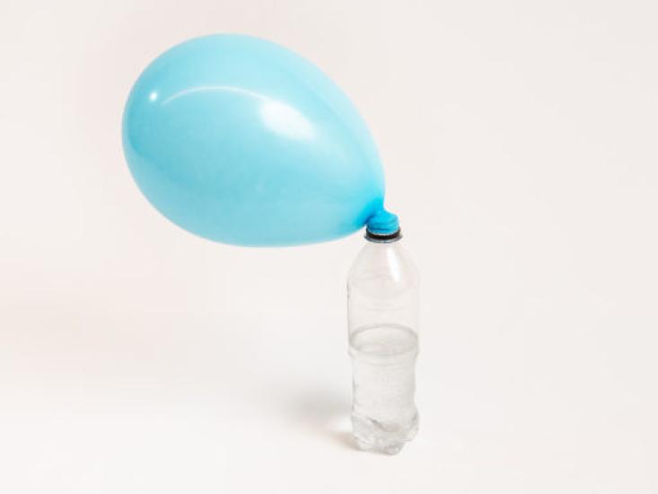 A blue balloon attatched to an empty water bottle is inflated by the gases that were created in the bottle.