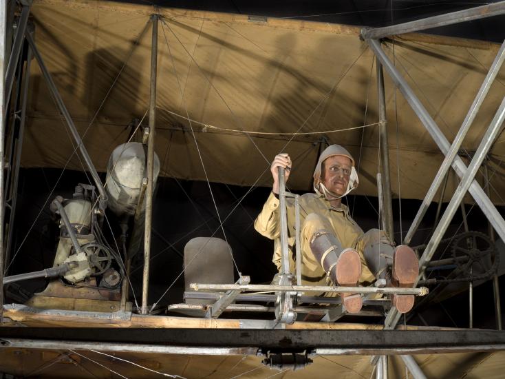 A pilot sits exposed on the lower wing of a vintage aircraft.