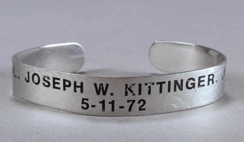 A simple cuff-style bracelet made from a silver-colored metal. Engraved across the bracelet in black letters is Joseph W. Kittinger and the date 5-11-72.