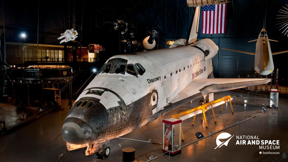 In a hangar dedicated to space artifacts at the Steven F. Udvar-Hazy Center, a space shuttle sits front and center. Space Shuttle Discovery looks like an oversized plane and its white paneling shows the wear and tear of flying in space. 