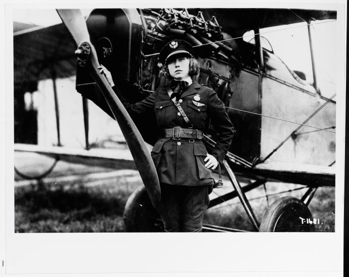 A woman standing beside an aircraft, appearing confident in a pilot's uniform and cap.