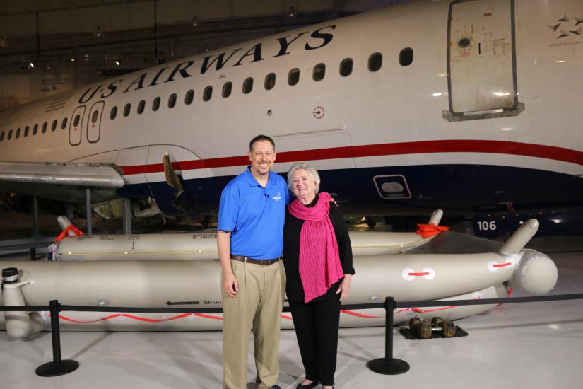 Two people stand in front of an aircraft. 