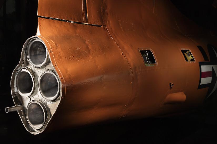 Side view of engine of an aircraft with three exhaust valves. The aircraft is painted orange. 