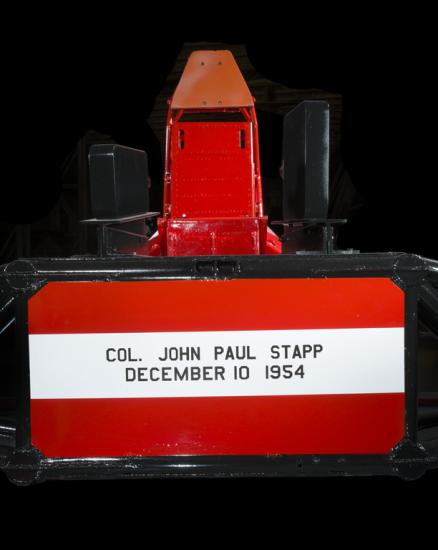 Straight metal seat attached to the middle of a rocket sled. Col. John Paul Stapp December 10 1954 is painted on the seat. 