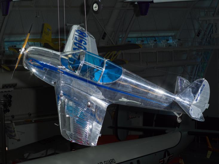 Metal plane with wood propeller and blue-tinted windows hanging in the museum. 